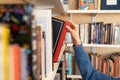 Woman hand picking book from bookshelf in library in university, college, high school or bookshop Royalty Free Stock Photo