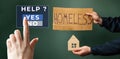 Female hand push a virtual button to the help. A man hold a cardboard house and sign with the inscription HOMELESS. Dark