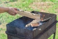 Female hand put birch firewood into bbq grill. Camping, cooking outdoors