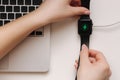 Female hand put smart watch on wireless charging with on-screen charging indicator. Work place near at the laptop. Top Royalty Free Stock Photo