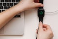 Female hand put smart watch on wireless charging with on-screen charging indicator. Work place near at the laptop. Top Royalty Free Stock Photo