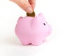Female hand putting a coin into piggy bank on white isolated background. Pink piggy bank Royalty Free Stock Photo
