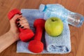 Female hand with red dumbbell and fresh green apple and water bottle on blue towel on wooden floor Royalty Free Stock Photo