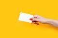 Female hand with red manicure holding blank white business card, close-up, isolated on yellow background Royalty Free Stock Photo