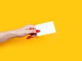 Female hand with red manicure holding blank white business card, close-up,  on yellow background Royalty Free Stock Photo