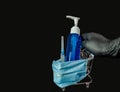 A female hand in a rubber glove holds the handle of a decorative trolley with a protective medical mask, a syringe, soap in a bank