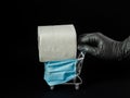 Female hand in a rubber glove rolls a decorative trolley in a protective medical mask, toilet paper on a black background