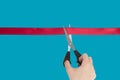 Female Hand scissors cuts a red ribbon. Isolate on a blue background