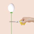 Female hand with scissors and egg like balloon