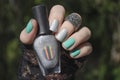 Female hand with short nails and turquoise gray holographic manicure holds a bottle of nail polish