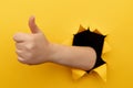 Female hand showing a thumb up sign through a ripped hole in yellow paper wall. Well done, good job concept Royalty Free Stock Photo