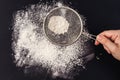 Female hand sifts flour on a black background