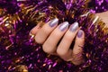 Female hand with silver Christmas nail design. Silver nail polish manicure. Female hand holding purple New Year tinsel