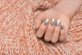 Female hand with silver nail design. Silver nail polish manicured hand. Woman hand on orange wool shawl