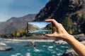 Female hand with smartphone close-up. Taking photo on smartphone while traveling. Delightful mountain landscape, stormy river Royalty Free Stock Photo