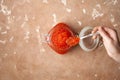 Female hand with a spoon with red caviar over an open glass jar filled with red caviar to the top on a beige textured stone Royalty Free Stock Photo