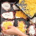 Female hand sprinkles with grated cheese the raw pork chops laying on a black baking tray. Process of cooking. Royalty Free Stock Photo