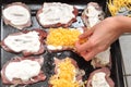 Female hand sprinkles with grated cheese the raw pork chops laying on a black baking tray. Process of cooking. Royalty Free Stock Photo