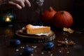 Female hand sprinkles powdered sugar on pumpkin cheesecake. Pumpkins, table lamp, foliage, vanilla on a wooden dark