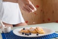 Female hand sprinkling powdered sugar on traditional syrniki or cottage cheese pancakes with blueberries and honey