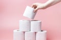 Female hand stacks toilet paper in a stack on pink background close-up.