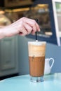 Female hand stirring a straw on a greek cold coffee, freddo cappuccino, outdoors Royalty Free Stock Photo