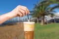 Female hand stirring a straw on a greek cold coffee, freddo cappuccino, outdoors Royalty Free Stock Photo