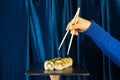 Female hand with sushi and wooden chopsticks set against a deep blue background with a curtain. Asian restaurant menu Royalty Free Stock Photo