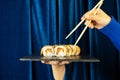 Female hand with sushi and wooden chopsticks set against a deep blue background with a curtain. Asian restaurant menu Royalty Free Stock Photo