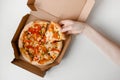 Female hand take piece of mexican pizza in cardboard box for delivery on white solid background