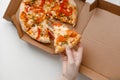 Female hand take piece of mexican pizza in cardboard box for delivery on white solid background