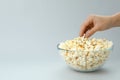 Female hand take popcorn from bowl on light gray background