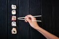 Female hand takes chopsticks sushi rolls with Chinese chopsticks. Lying on a black wooden board. View from above Royalty Free Stock Photo