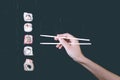 Female hand takes chopsticks sushi rolls with Chinese chopsticks. Lying on a black wooden board. View from above Royalty Free Stock Photo