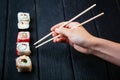 Female hand takes chopsticks sushi rolls with Chinese chopsticks. Lying on a black wooden board. View from above Royalty Free Stock Photo