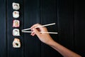 Female hand takes chopsticks sushi rolls with Chinese chopsticks. Lying on a black wooden board. View from above Royalty Free Stock Photo