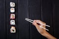 Female hand takes chopsticks sushi rolls with Chinese chopsticks. Lying on a black wooden board. View from above Royalty Free Stock Photo