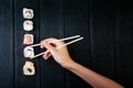 Female hand takes chopsticks sushi rolls with Chinese chopsticks. Lying on a black wooden board. View from above Royalty Free Stock Photo