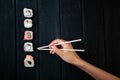 Female hand takes chopsticks sushi rolls with Chinese chopsticks. Lying on a black wooden board. View from above Royalty Free Stock Photo