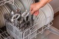 Female hand takes clean utensils from dishwasher