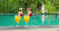 Female hand takes a cool cocktail near to swimming pool. Couple of glasses of orange juice on blue water background. Summer day Royalty Free Stock Photo