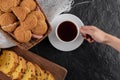 Female hand taking cup of tea. Black background with fresh homemade cookies Royalty Free Stock Photo