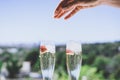 Female hand throwing ice into a glasses champagne with strawberry inside on sunny terrace overlooking swimming pool at Royalty Free Stock Photo