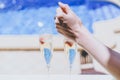 Female hand throws ice into a glass champagne with strawberry on sunny terrace overlooking swimming pool at summer day Royalty Free Stock Photo