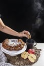 A female hand is about to dip a slice of donut into a smoking hot drink