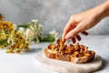 Female hand and toast with fried chanterelles, on marble countertop with flowers in the background. Generative AI