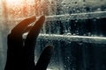 female hand touching water droplets on the window in the rainy