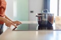 Female hand turning on induction stove with steel cooking pan in kitchen Royalty Free Stock Photo