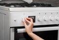 Female hand turning on white kitchen gas stove on gray Royalty Free Stock Photo