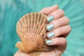 Female hand with vacation nail design. Glitter aquamarine nail polish manicure. Female hand hold sea shell